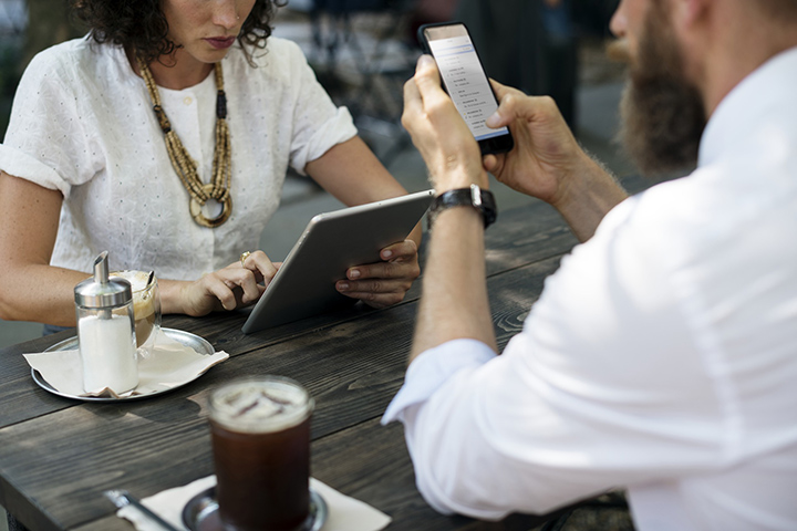 a person working on her tablet and another person working on his smartphone